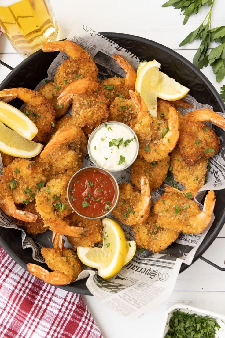 fried shrimp with dipping sauce and lemon wedges on a platter next to two glasses of beer