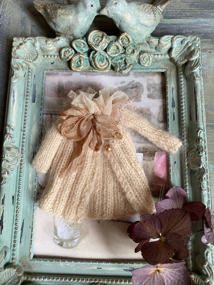 an old frame with a doll in it and flowers on the table next to it