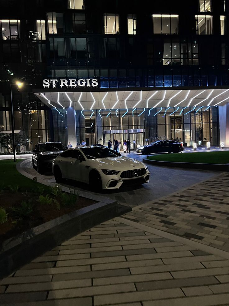 two cars parked in front of a building at night with the word stregis on it