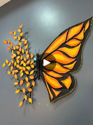 an orange butterfly with black wings and yellow flowers on it's back end, mounted to a gray wall