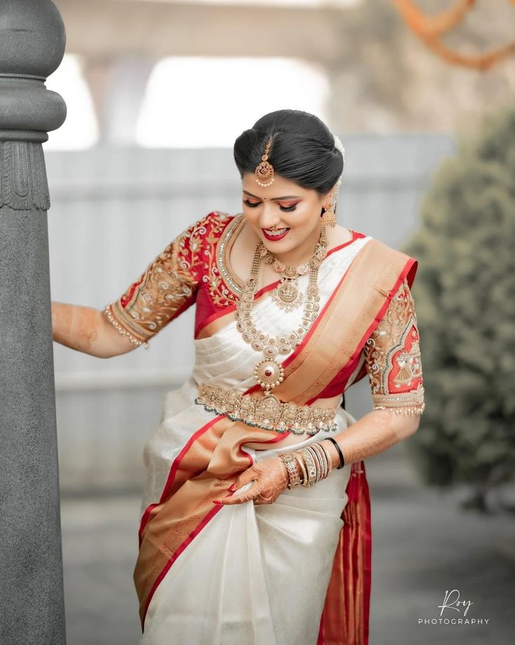 a woman in a red and white sari is standing near a pillar with her hands on the wall