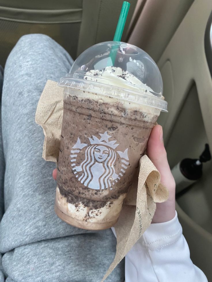 a person holding up a starbucks drink in their hand while sitting in the back seat of a car