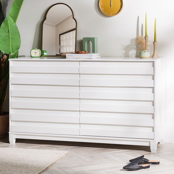 a white dresser sitting next to a mirror and plant