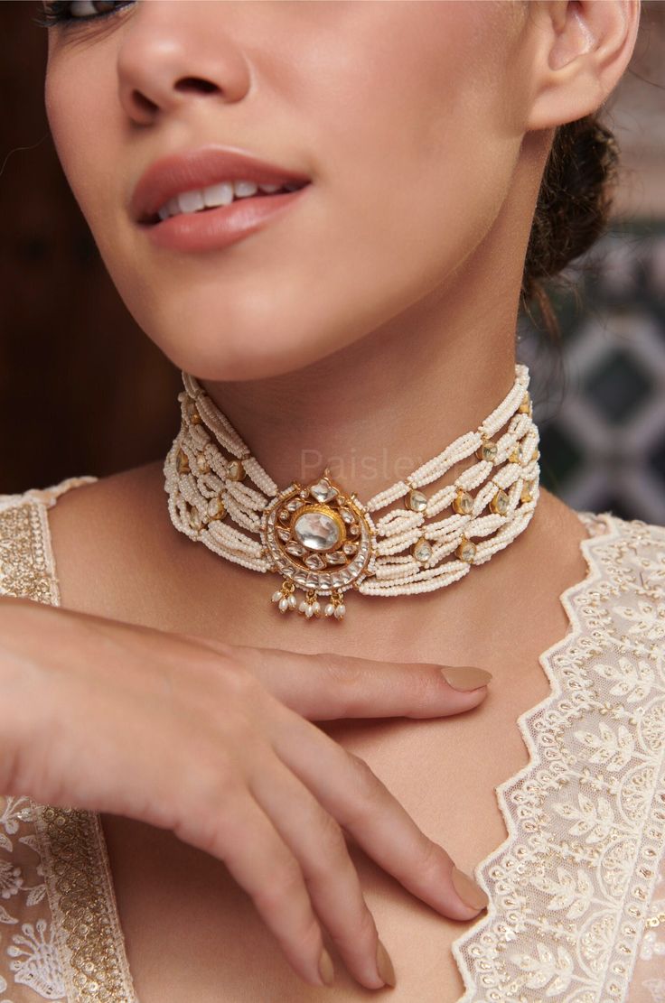 A work of art in jewelry, our Indian Bridal Kundan Choker Necklace captures the essence of celestial beauty and feminine grace. The centerpiece showcases a crescent moon motif, encrusted with Kundan, reflecting the radiance of the night sky strewn in luminous pearls. Every detail in this traditional pearl choker is inspired by the Sabyasachi Jewelry. From the delicate placement of pearls to the celestial motif,  the gold-plated necklace embodies a sense of celestial enchantment, inviting you to embrace the timeless beauty of the moon. Necklace- Adjustable Dori Weight- 57 gm Paisley Pop travels the depths of India to learn techniques and crafts from deep down in the local markets and villages. We give utmost importance to our quality and packaging. Our goal is to make sure you receive exact Ceremonial Temple Jewelry With Motifs, Fusion Style Gold Beaded Jewelry, Fusion Gold Beaded Jewelry, Handmade White Temple Jewelry Bridal Necklace, Handmade White Bridal Temple Jewelry Necklace, Handmade White Temple Jewelry, White Round Necklaces For Festivals, Festive White Fusion Jewelry, Festive Fusion White Jewelry