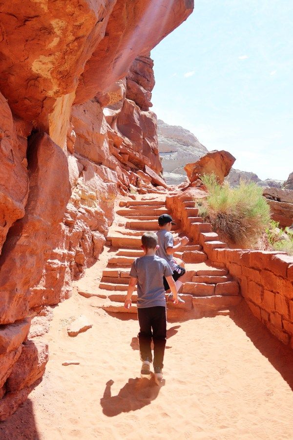 two people are walking up some stairs in the desert with red rocks and green grass