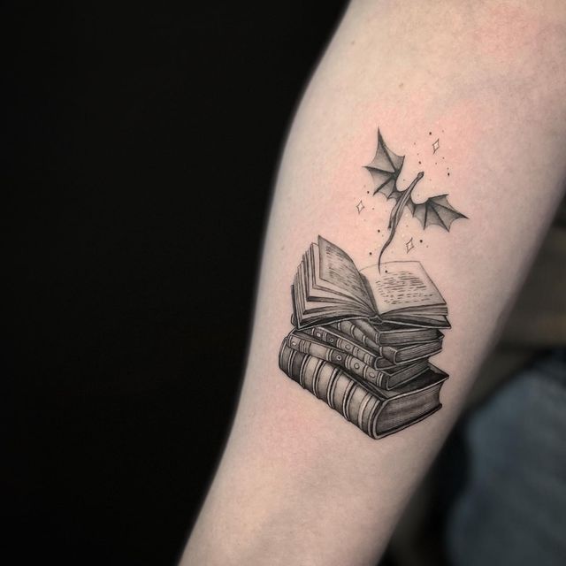 a black and white photo of a book tattoo on the left arm with stars coming out of it