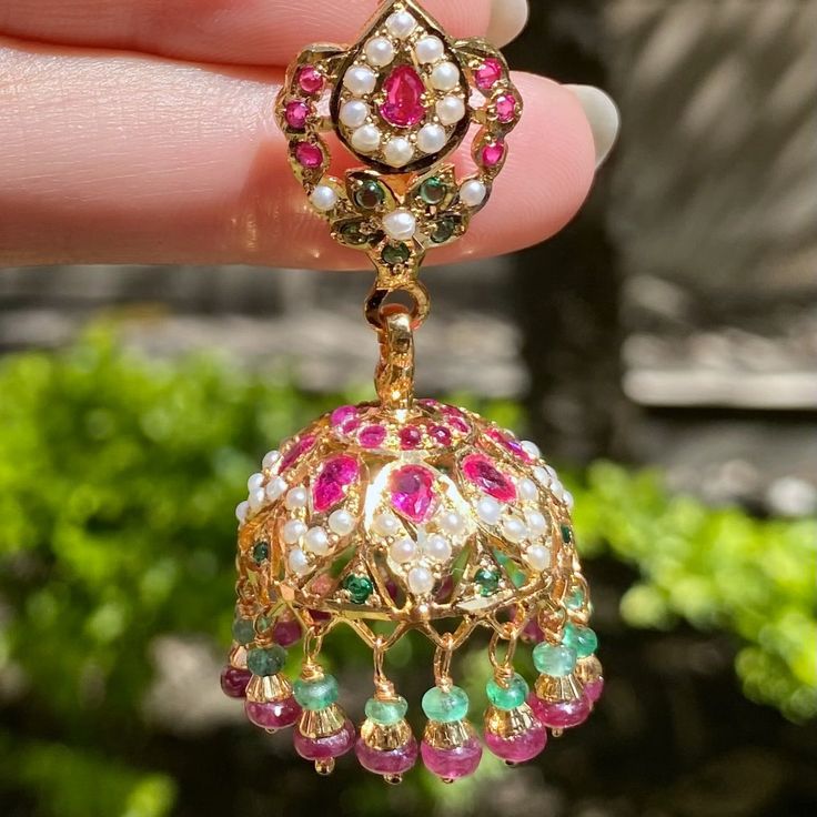 Featuring a pair of jadau jhumkas studded with freshwater pearls, ruby like red stones and emerald like green stones. The hangings comprise genuine rubies and emerald beads. The earrings close with a bombay screw.