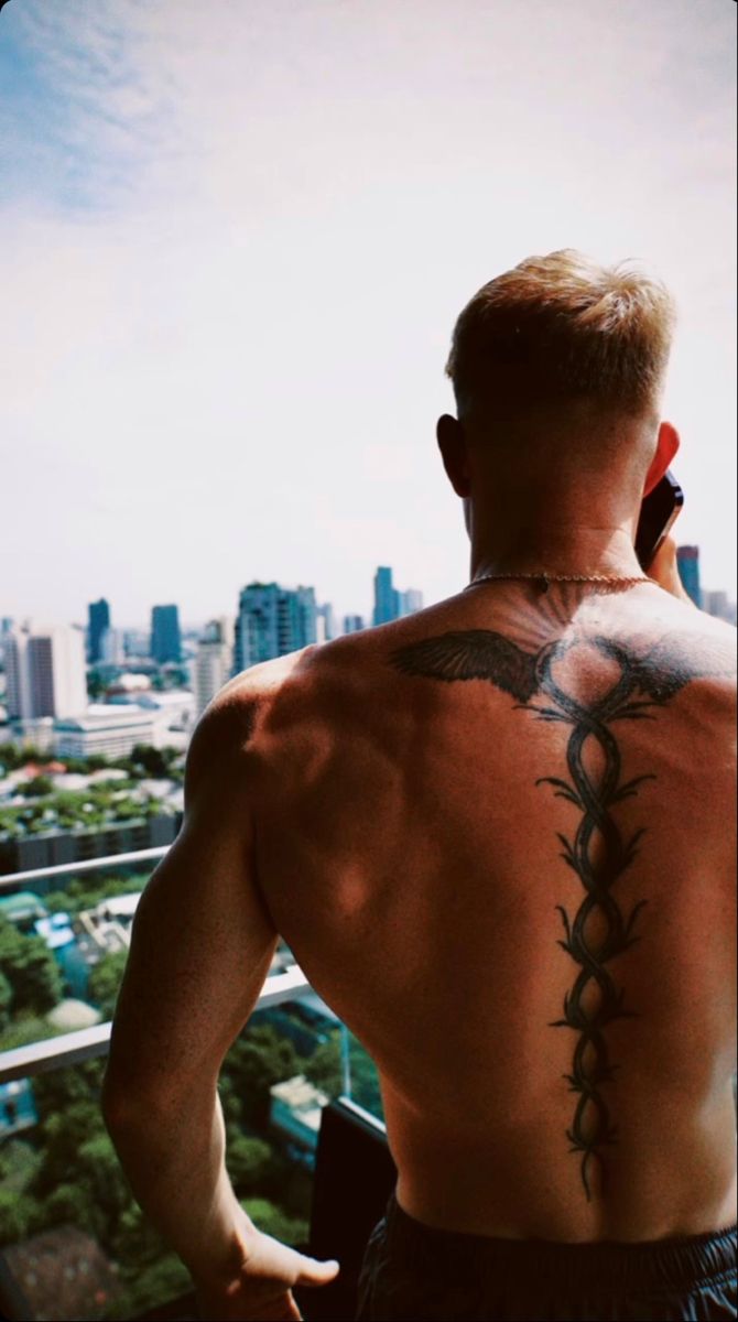 a man with a tattoo on his back looking at the city from a high rise