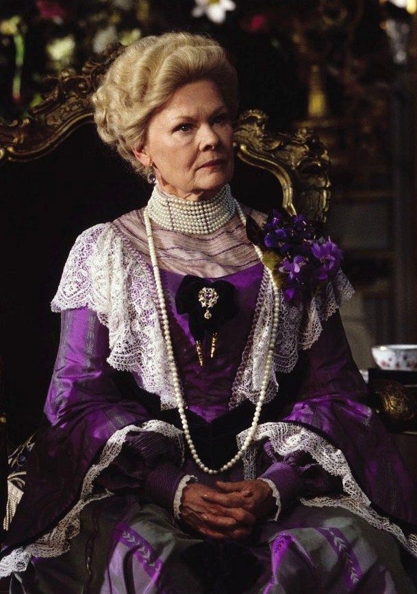 there is a woman sitting in a chair with pearls on her neck and purple dress