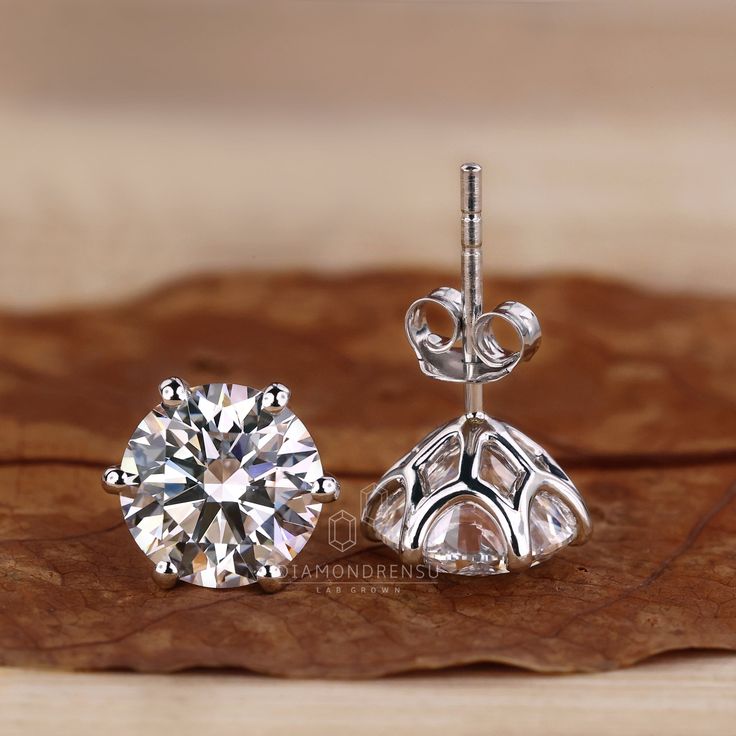 a pair of diamond earrings sitting on top of a wooden table next to a leaf