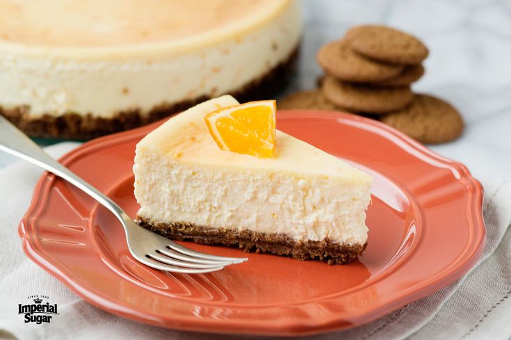 a slice of cheesecake on a red plate with a fork and cookies in the background