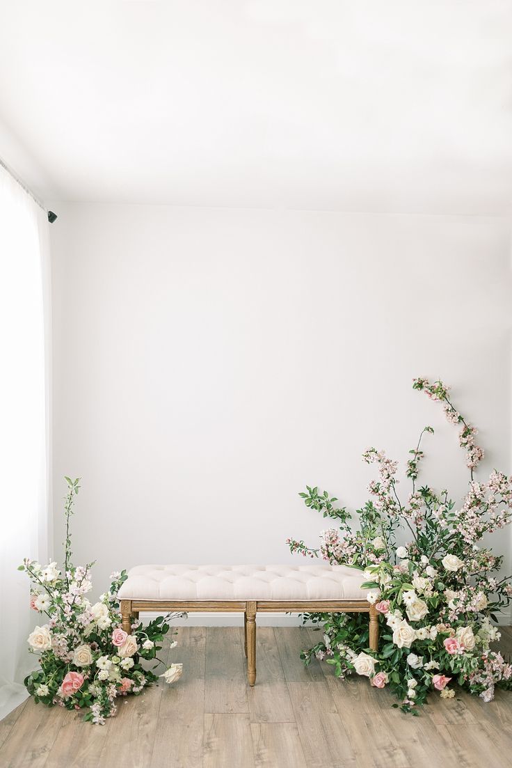 two benches with flowers on them in front of a white wall and wood flooring