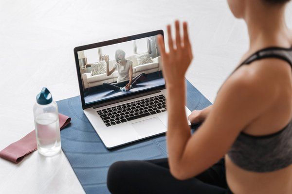 a woman sitting in front of a laptop computer on top of a blue yoga mat