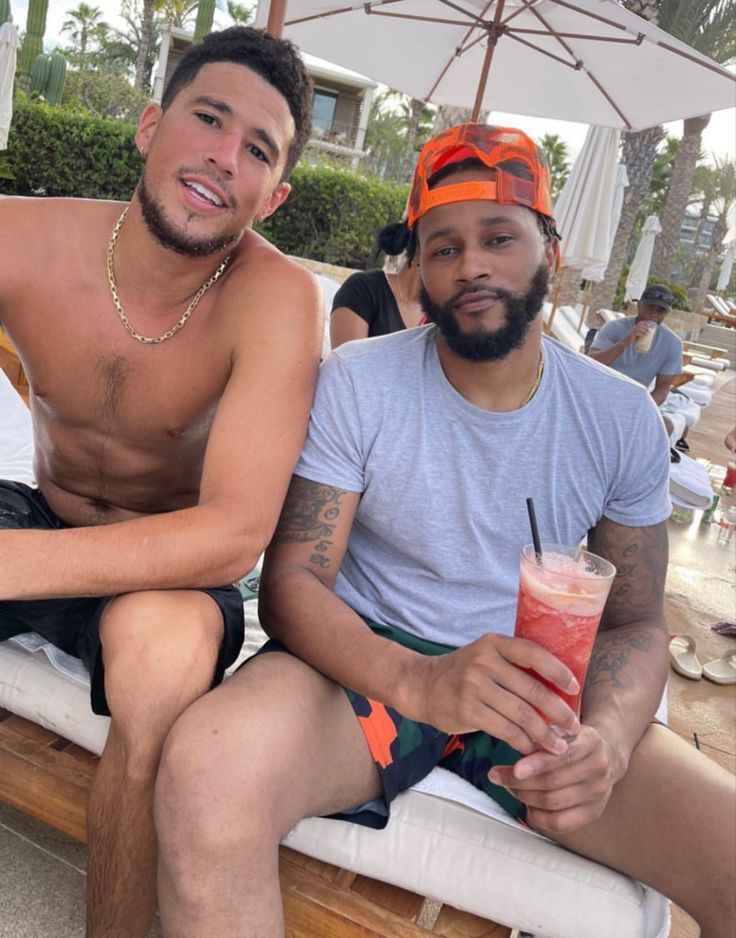 two shirtless men sitting on a bench with drinks in their hands and one holding a drink