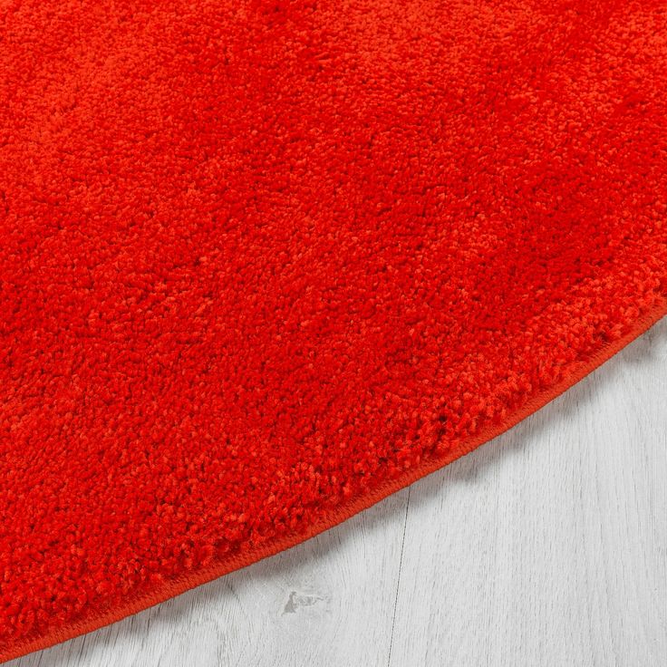 a bright red rug on the floor with white wood floors in the background and an orange area rug