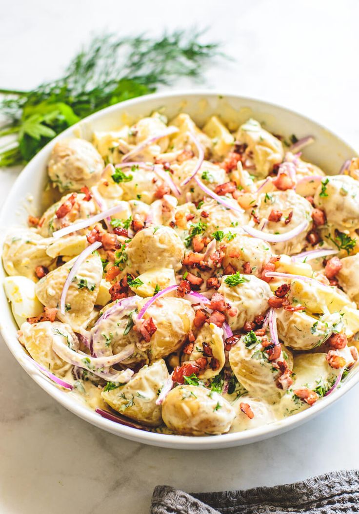 a bowl filled with pasta and vegetables on top of a white counter next to a pair of mitts