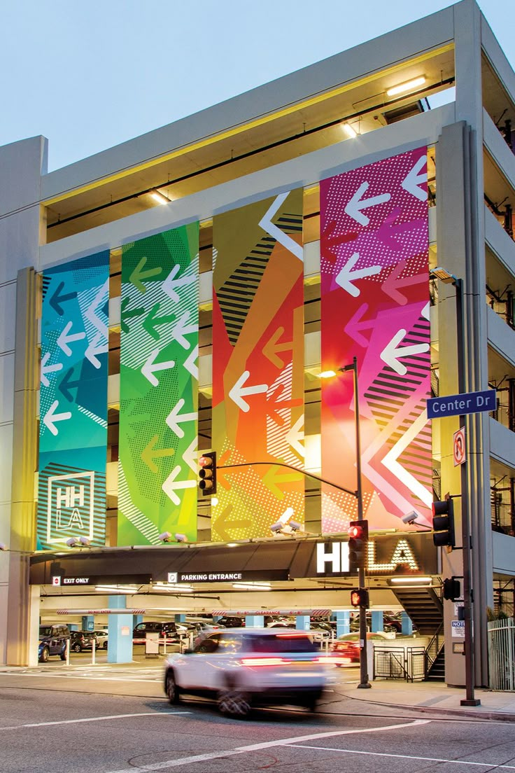 a car driving past a multicolored building on a city street with traffic lights