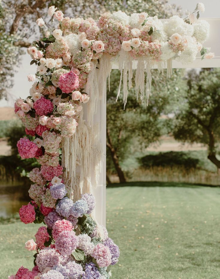 an outdoor wedding ceremony with flowers hanging from the ceiling and draping over it