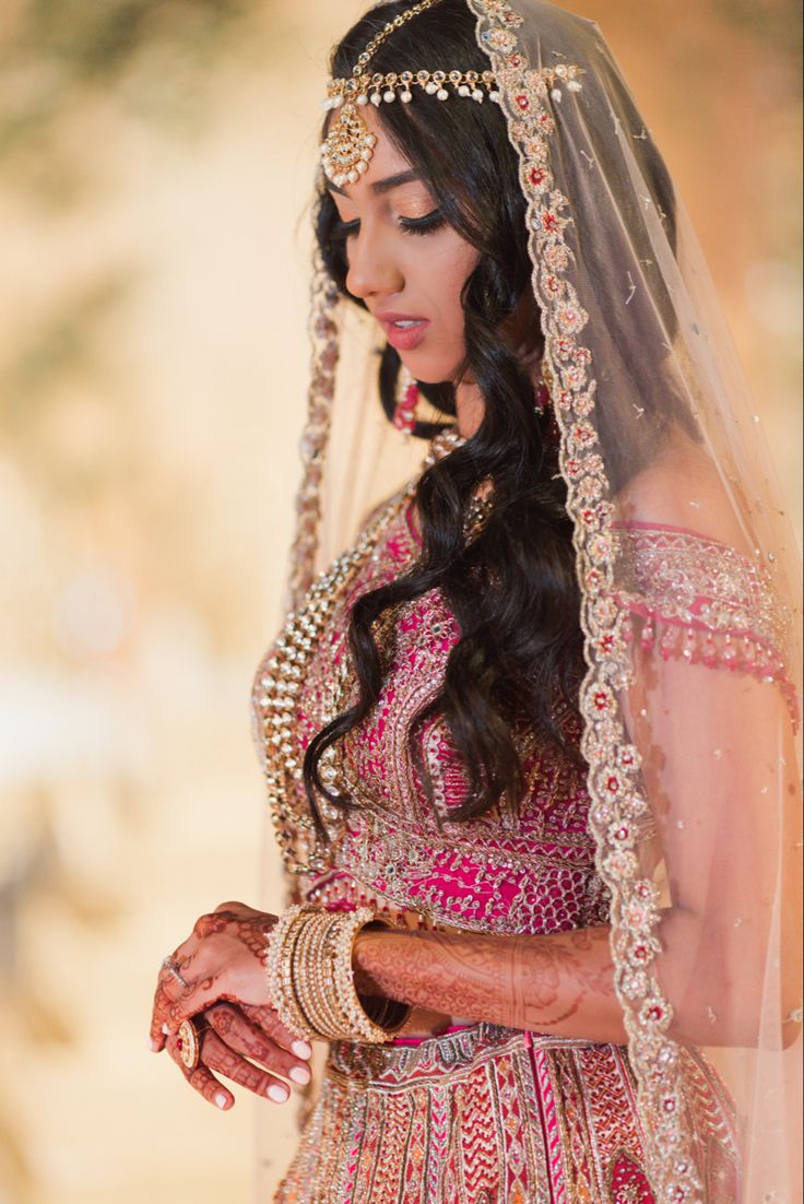 a woman in a pink and gold wedding dress holding her hands together while wearing a veil