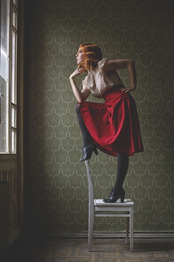 a woman sitting on top of a chair in front of a window