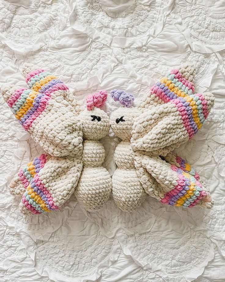 two crocheted teddy bears laying next to each other on a white bed sheet