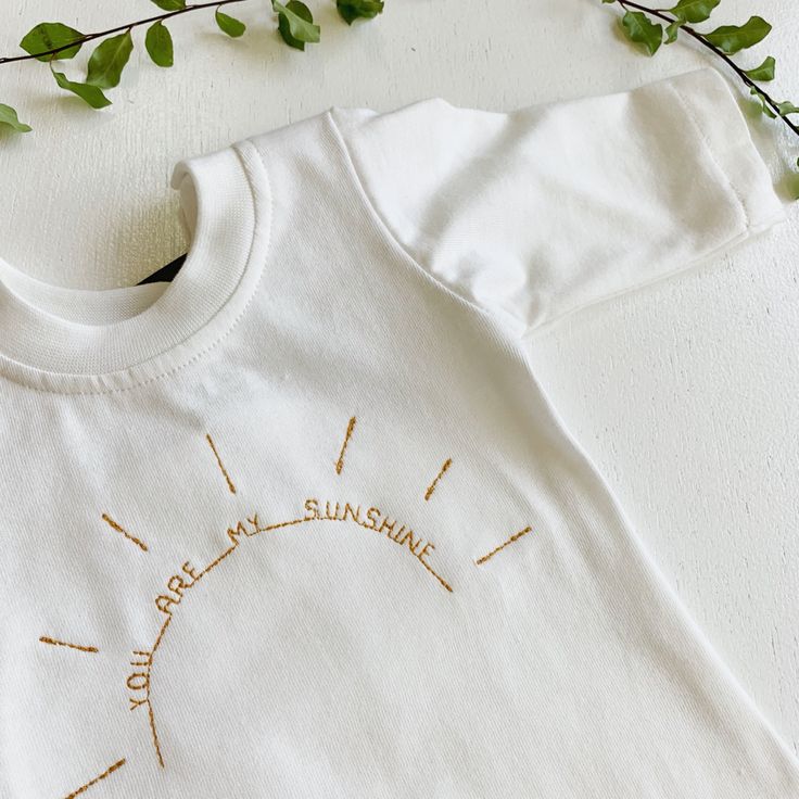 a white t - shirt with the words relax and shine on it next to some green leaves