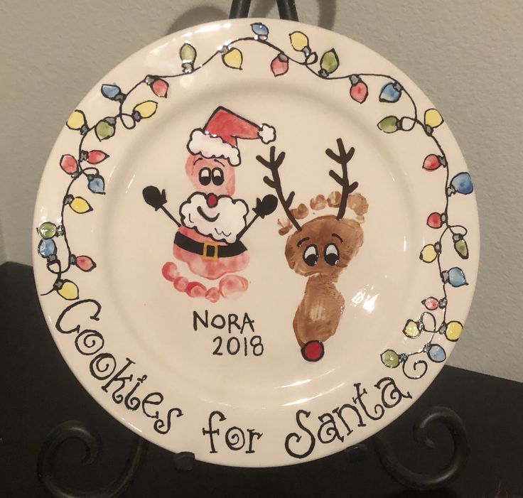 a white plate with a reindeer and santa clause painted on it's side, hanging from a hook