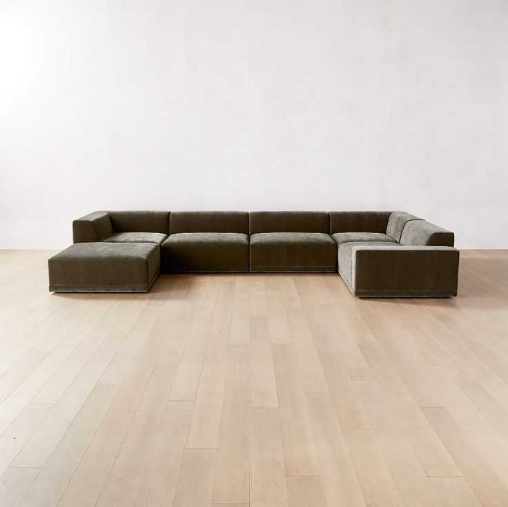 a large sectional couch sitting on top of a hard wood floor next to a white wall