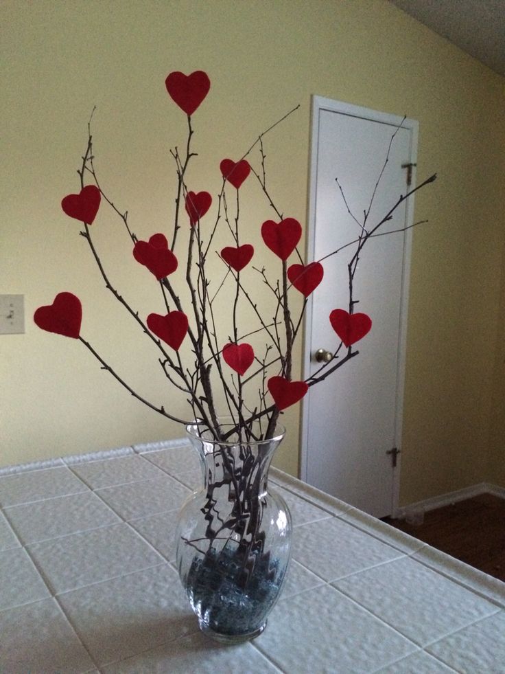 a vase filled with branches and hearts on top of a white tablecloth covered table