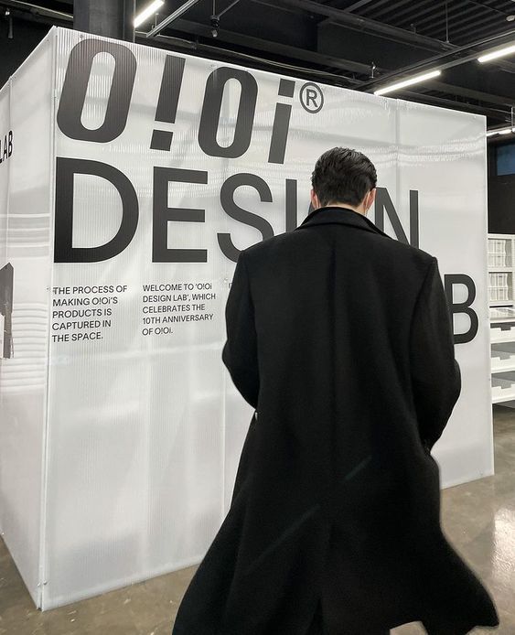 a man in a black coat is walking by a white sign with the words design on it