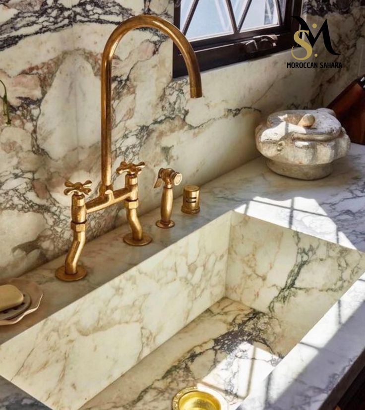 a marble sink with gold faucets in the middle and windows above it, next to a window sill