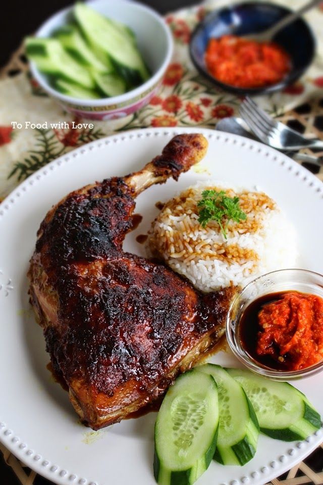 a white plate topped with meat and rice next to cucumbers on a table