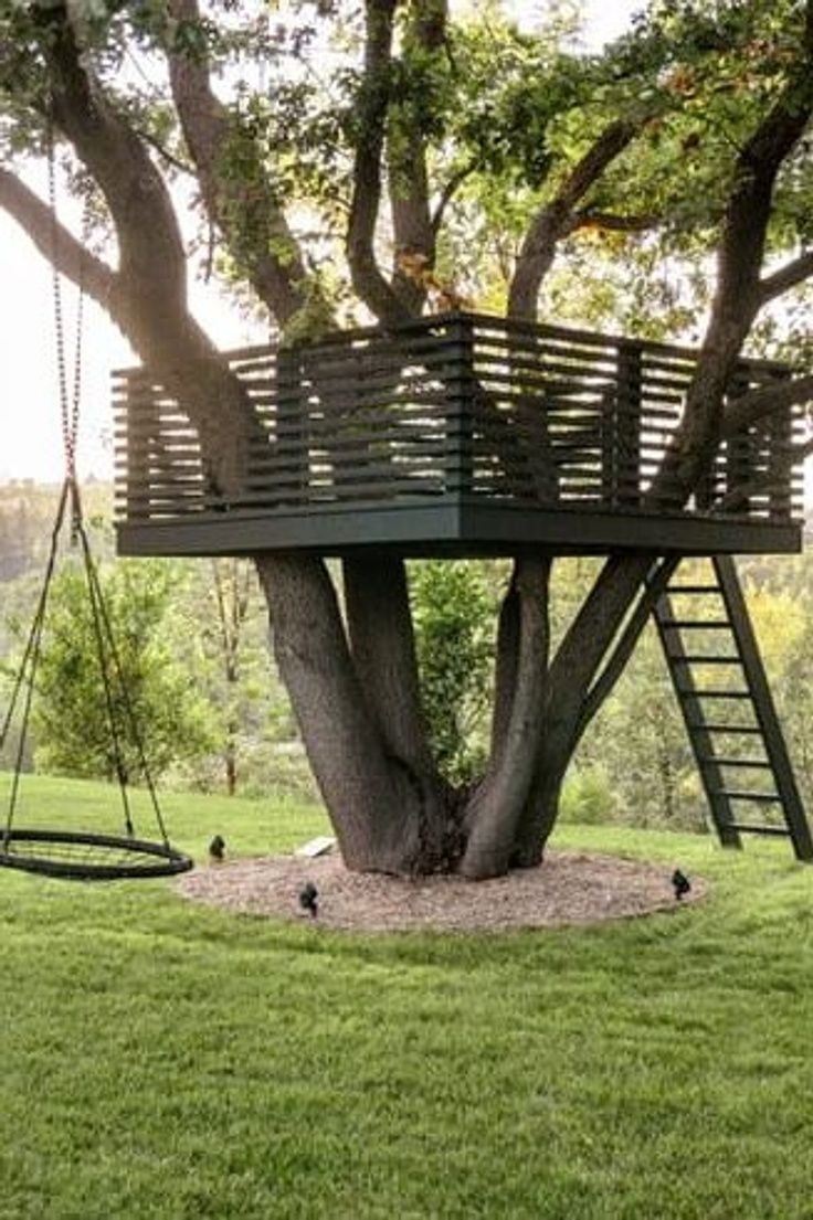 a tree house that is in the middle of a grassy area with a swing set attached to it