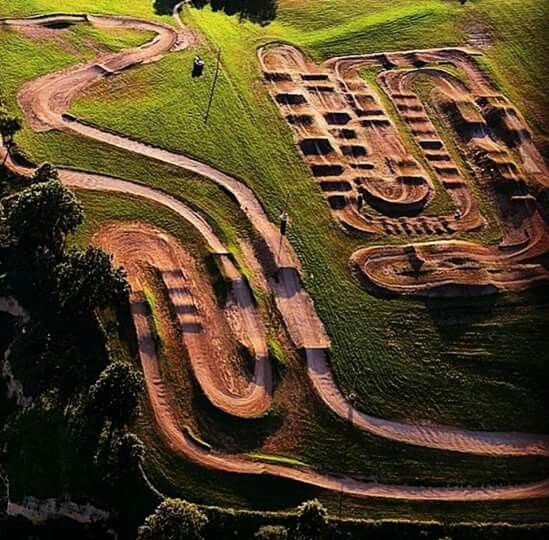 an aerial view of a dirt track in the middle of a green field with trees