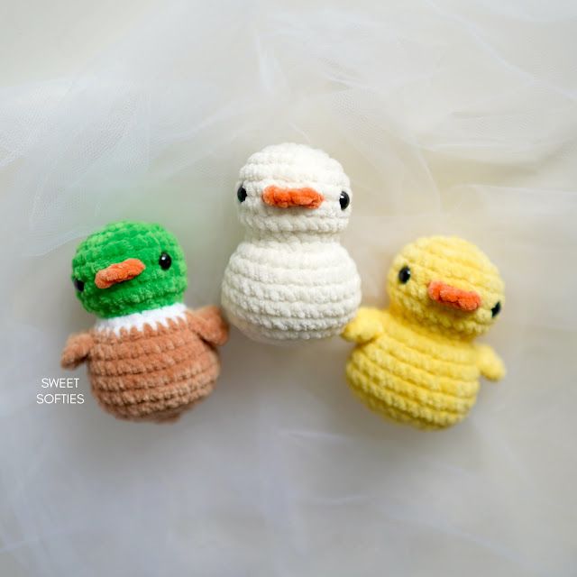 three small crocheted ducks sitting next to each other on a white surface,