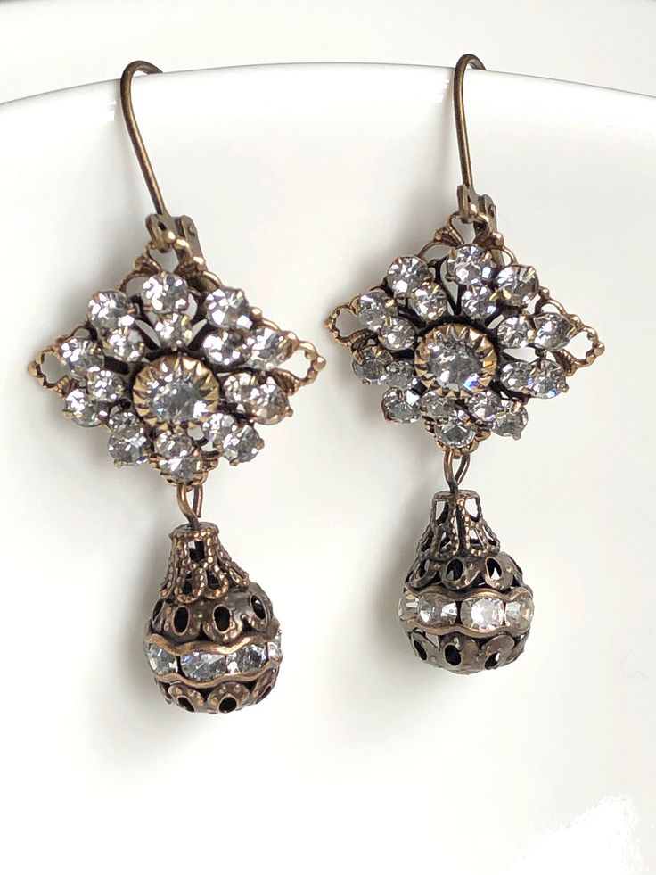 "These earrings from the 1920s style is the perfect addition to your art deco jewelry or can be used for a Gatsby themed wedding. Give these art deco earrings as a birthday gift, girlfriend gift, or a present for mom. Add glamour and sparkle to any outfit with these crystal dangle earrings for women and enjoy free shipping! Gorgeous styled 1920s earrings feature beautiful 3 tiered layers of clear Swarovski crystals which are affixed to diamond shaped antiqued brass filigree settings. Antique brass filigree and crystal teardrops dangle from each diamond shaped setting. The sparkle and shine on these art deco earrings is quite brilliant. Antique brass leverback ear wires complete these Swarovski crystal earrings.  These earrings would be perfect as art deco wedding jewelry, formal earrings, Dangle Art, Flapper Accessories, Swarovski Jewelry Earrings, Vintage Statement Earrings, 1920s Wedding, Crystal Earrings Wedding, Crystal Bridal Earrings, Special Occasion Jewelry, Glass Drop Earrings