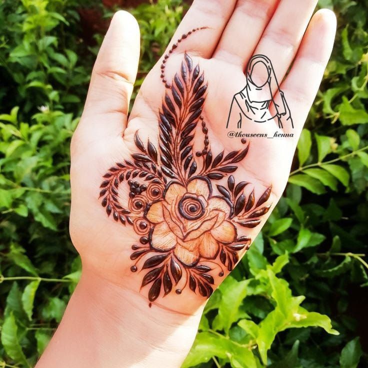 a woman's hand with a henna tattoo on it and some plants in the background