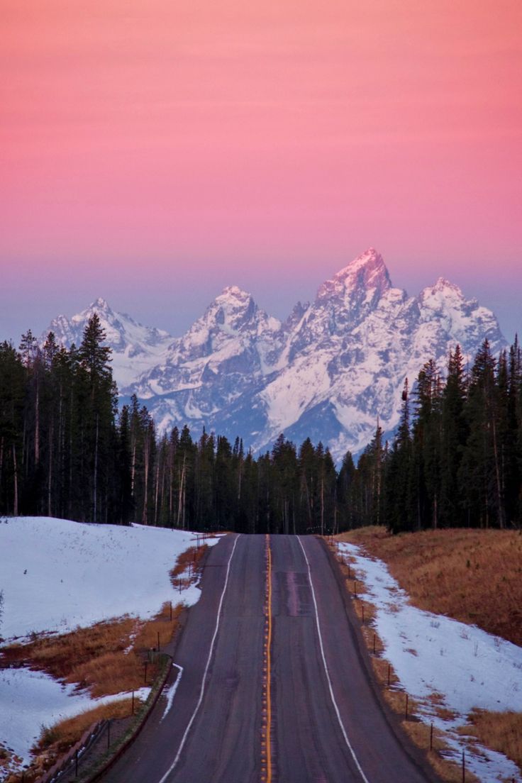 an empty road in front of snow covered mountains