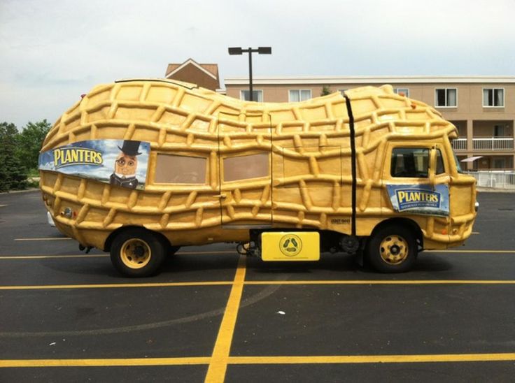 a large yellow truck is parked in a parking lot next to a tall building with an advertisement for planters on it's side