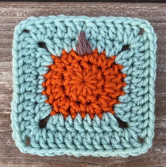 a crocheted square with an orange and blue design on it, sitting on a wooden surface