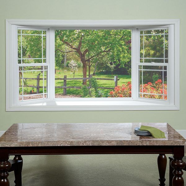 an empty table in front of two windows with the view of a park and flowers