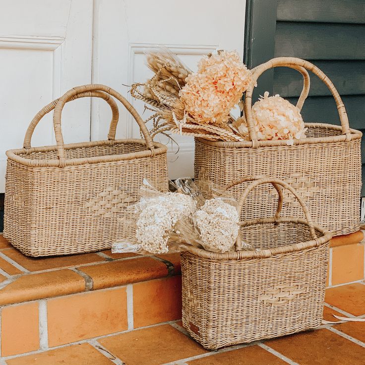 two wicker baskets sitting on top of a brick floor next to a door with flowers in them