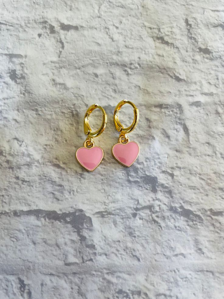 These cute and dainty gold-plated huggie earrings feature mini pink heart charms! Trendy Huggie Heart Earrings For Valentine's Day, Trendy Hypoallergenic Hoop Earrings For Valentine's Day, Pink Huggie Heart Earrings, Pink Heart Charm Huggie Jewelry, Pink Huggie Jewelry With Heart Charm, Pink Heart Huggie Earrings For Pierced Ears, Pink Huggie Heart Earrings For Pierced Ears, Pink Dainty Huggie Earrings, Pink Dainty Huggie Jewelry