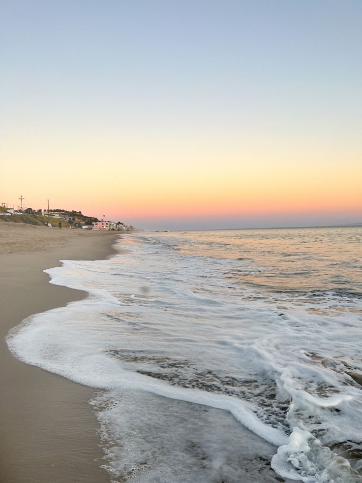 an ocean beach with waves coming in to the shore and houses on the other side