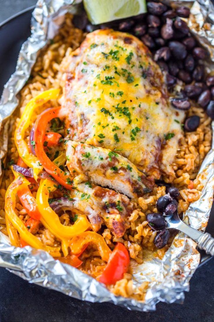 an enchilada covered in chicken, beans and rice with a lime wedge