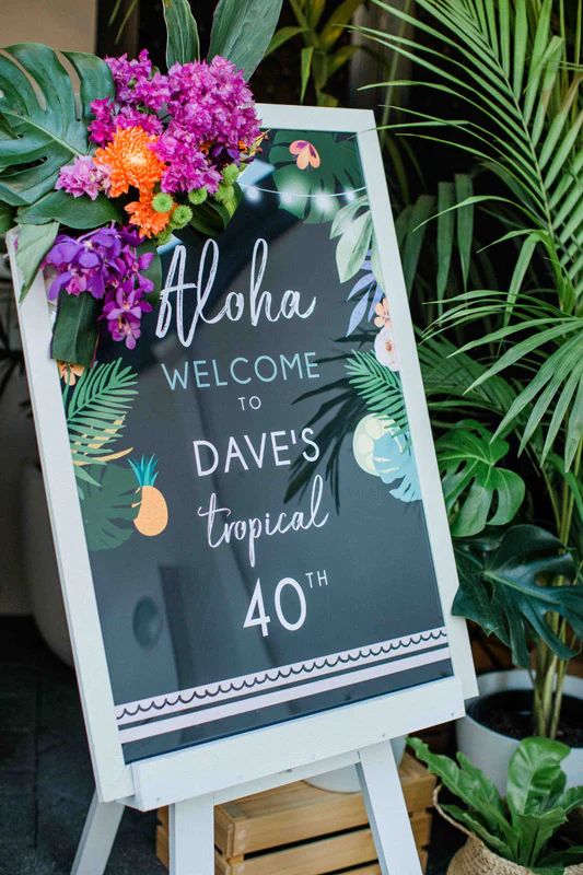 a welcome sign with flowers and greenery on it