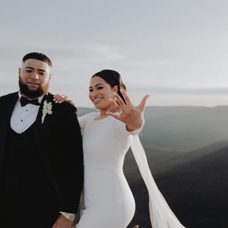 a bride and groom posing for a photo on top of a mountain with their hands in the air