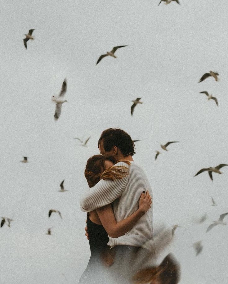 two people embracing each other with birds flying in the background