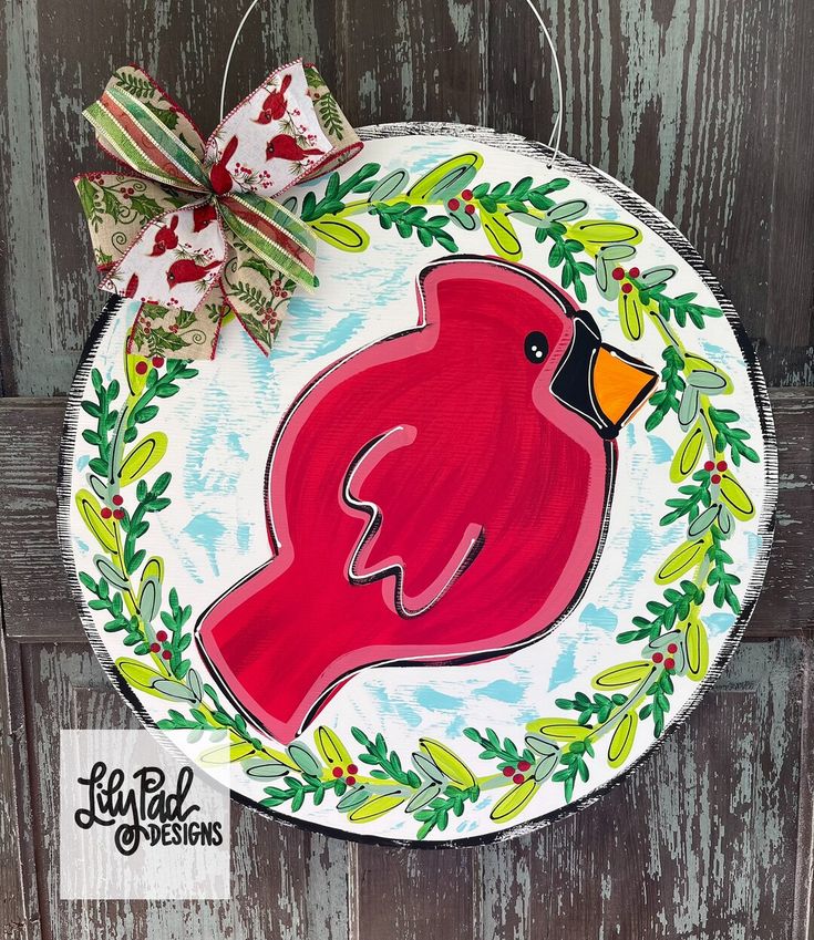 a red bird painted on a white plate with holly wreaths and bows hanging from it's side