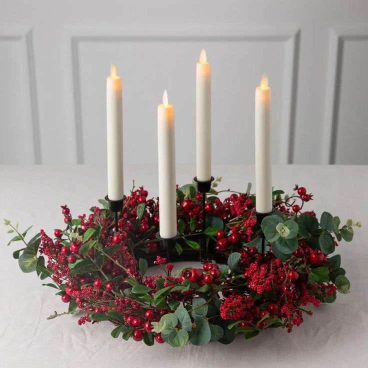 a wreath with candles on top of it and red berries in the center is surrounded by greenery